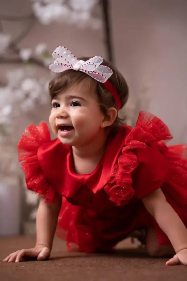Bebê sorrindo com vestido vermelho e laço rosa